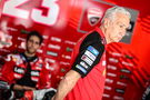 Davide Tardozzi stands in factory Ducati MotoGP garage with Enea Bastianini in the background. - Gold and Goose.