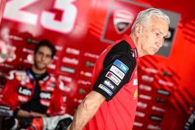 Davide Tardozzi stands in factory Ducati MotoGP garage with Enea Bastianini in the background. - Gold and Goose.